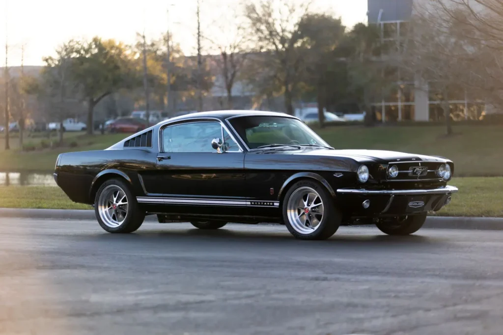 A side shot of a Black 1966 Mustang 2+2 Fastback with white stripes.