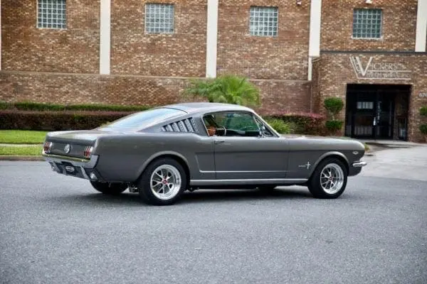 A side view of a 1966 Mustang 2+2 Fastback parked in front of “Vickers Metal Works inc.”