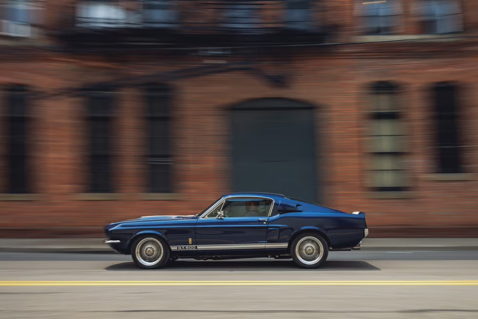 Side view of a 1967 Shelby GT 500 in motion on the road.