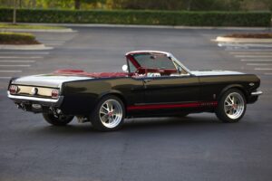 A lateral view of a black 1966 Mustang Convertible parked in a parking lot.
