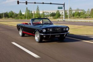 A man driving a 1966 Mustang Convertible on a road.