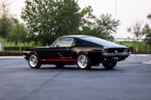 A lateral view of a black 1967 Mustang GT / GTA 2+2 Fastback with red stripes.