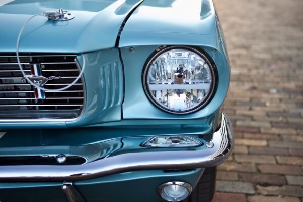 The front headlight of a baby blue 1966 Mustang Convertible.