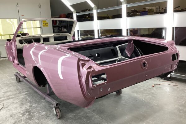 Pastel pink 1966 Mustang Convertible restoration in a garage.