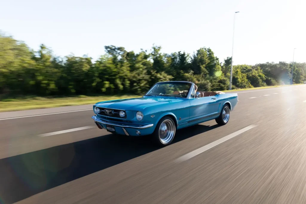 A man driving a 1966 Mustang Convertible on a road