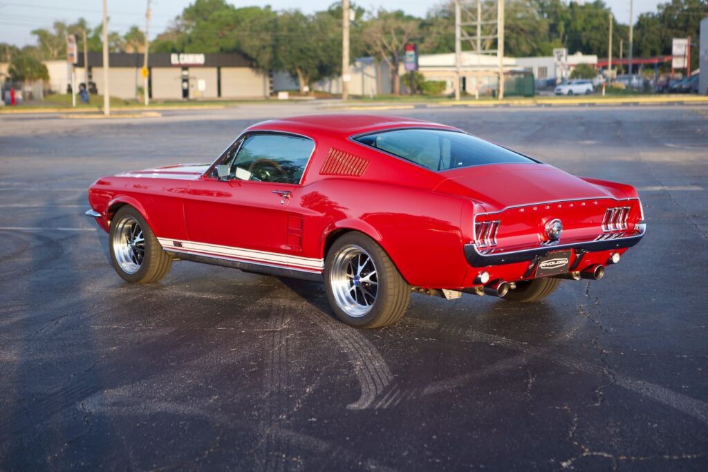 A lateral view of a red 1967 Mustang GT / GTA 2+2 Fastback parked in a parking lot.