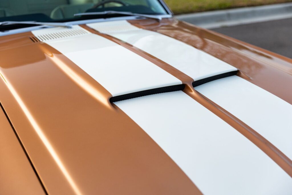 Macro view of the integrated fiberglass hood scoop on a Copper metallic 1967 Revology Shelby GT350 with white racing stripes.