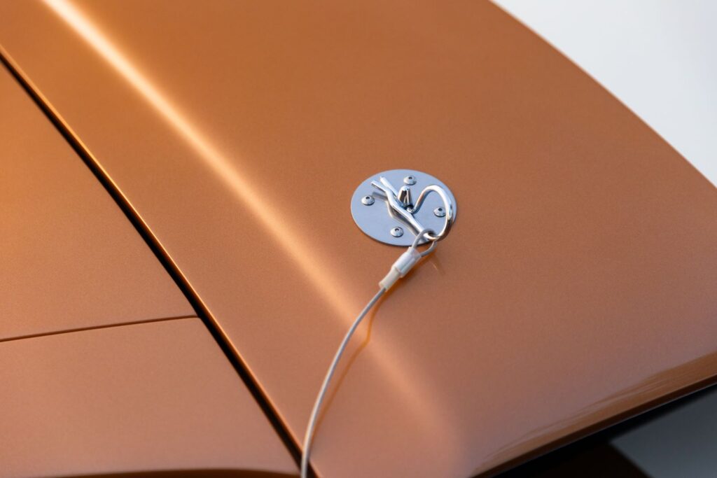 Extreme macro of a polished chrome hood pin and lanyard on the copper metallic fiberglass hood of a 1967 Revology Shelby GT350.