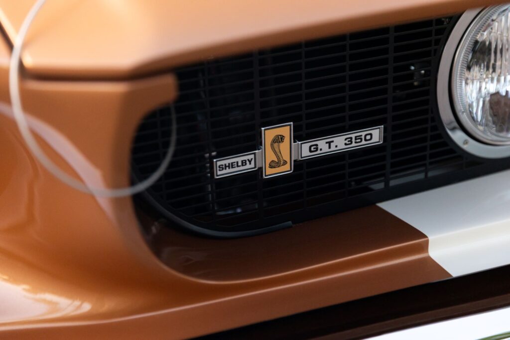Extreme close-up of the "Shelby G.T. 350" emblem with the Cobra snake logo mounted on the blacked-out grill of a copper metallic Revology Mustang.