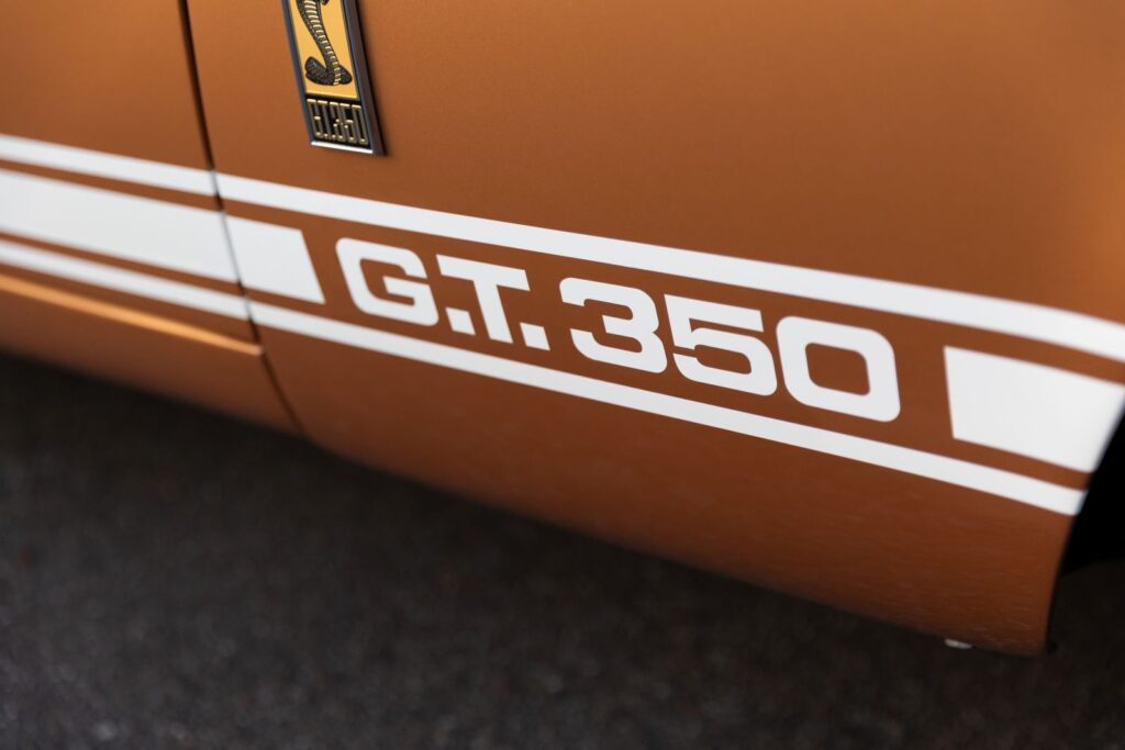 Close-up of the "G.T. 350" white rocker stripes and fender emblem on the Copper metallic body of a 1967 Revology Shelby reproduction.