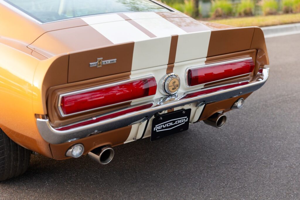 Rear view of a Copper metallic 1967 Revology Shelby GT350 showing the horizontal sequential taillights, integrated decklid spoiler, and dual exhaust tips.