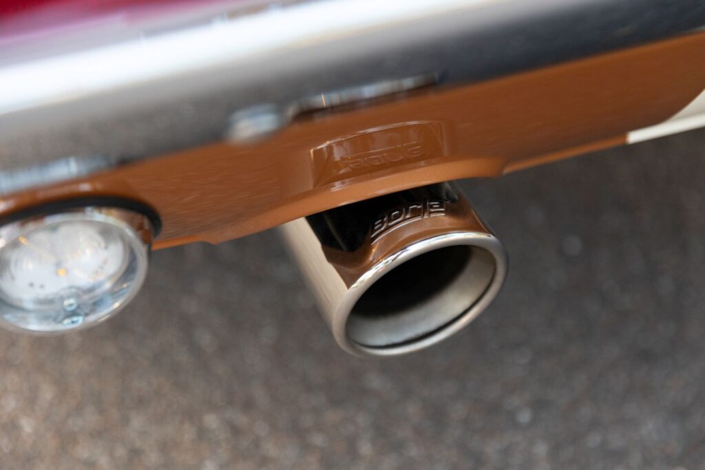 Extreme macro of a polished stainless steel exhaust tip integrated into the Copper metallic rear valance of a 1967 Revology Shelby GT350.
