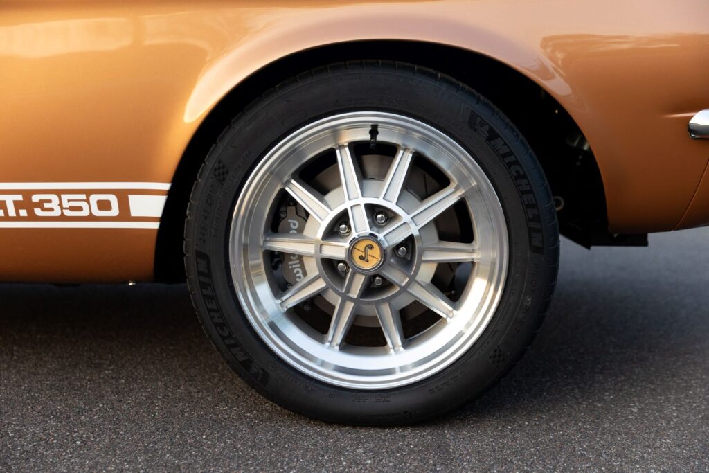 Side view of a 17-inch 10-spoke aluminum Shelby wheel with a Cobra center cap and Wilwood disc brakes on a Copper metallic 1967 Revology GT350.