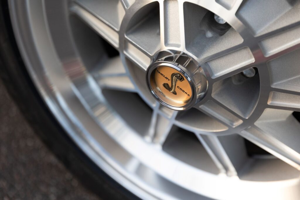 Extreme close-up of the polished chrome center cap with the golden Cobra snake logo on a 10-spoke aluminum wheel of a 1967 Revology Shelby GT350.