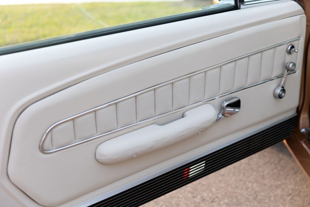 Interior view of an off-white leather Deluxe door panel with chrome trim and a horizontal door handle on a 1967 Revology Shelby GT350.
