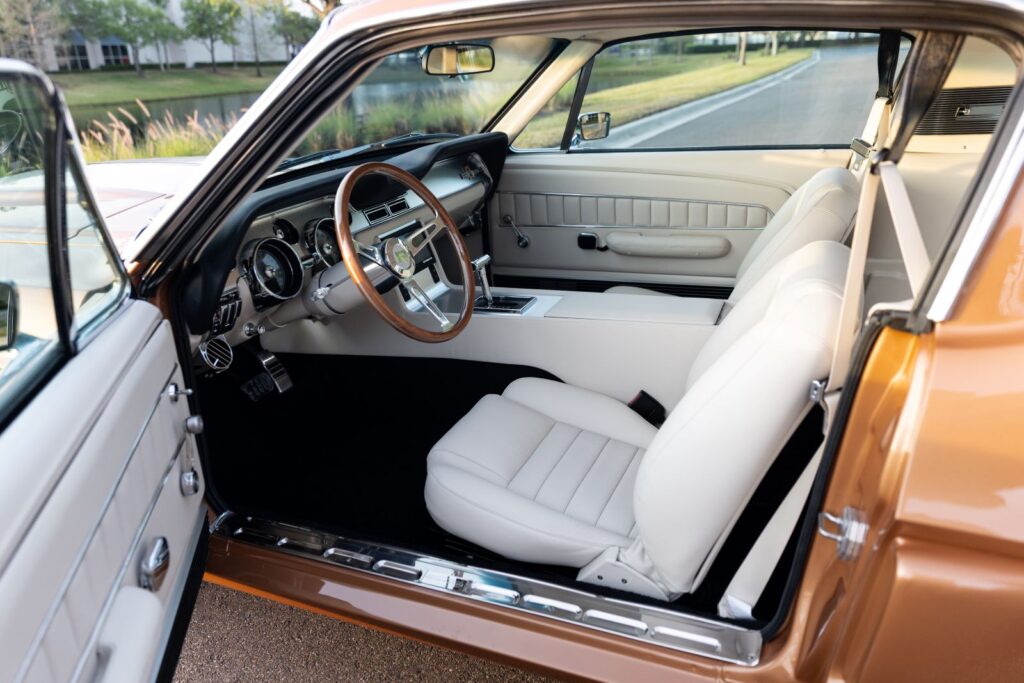 Full interior cabin view of a 1967 Revology Shelby GT350 featuring off-white leather sport seats, a wood-rim steering wheel, and a custom center console.