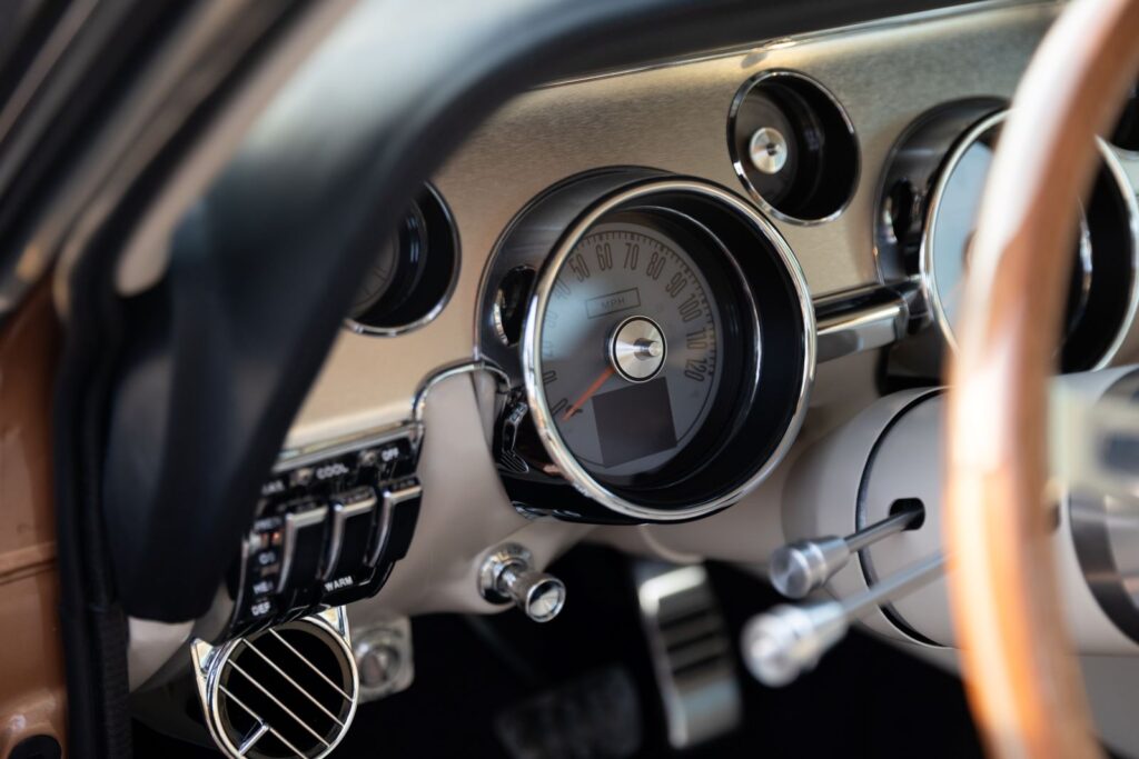 Close-up of the driver-side dashboard in a 1967 Revology Shelby GT350, featuring modern electronic gauges, chrome-bezel vents, and a vertical row of toggle switches.