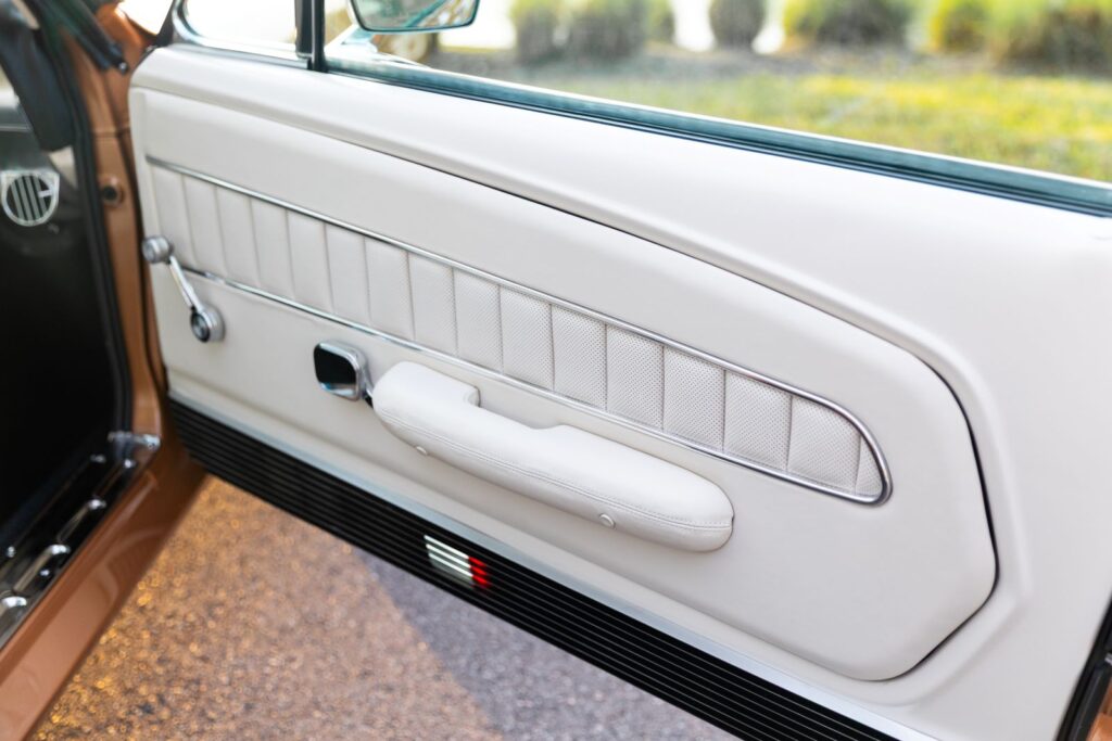 Interior view of the passenger-side Deluxe door panel in off-white leather with chrome accents and a black lower grille on a 1967 Revology Shelby GT350.