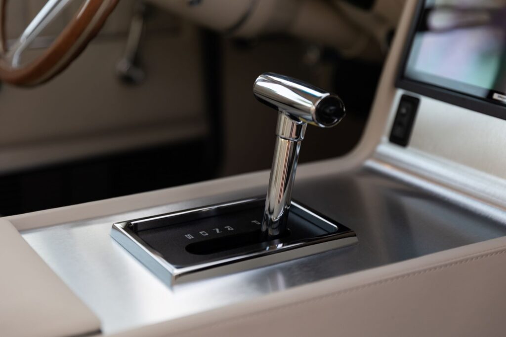 Close-up of a polished chrome T-handle automatic shifter integrated into a brushed aluminum and off-white leather center console in a 1967 Revology Shelby GT350.