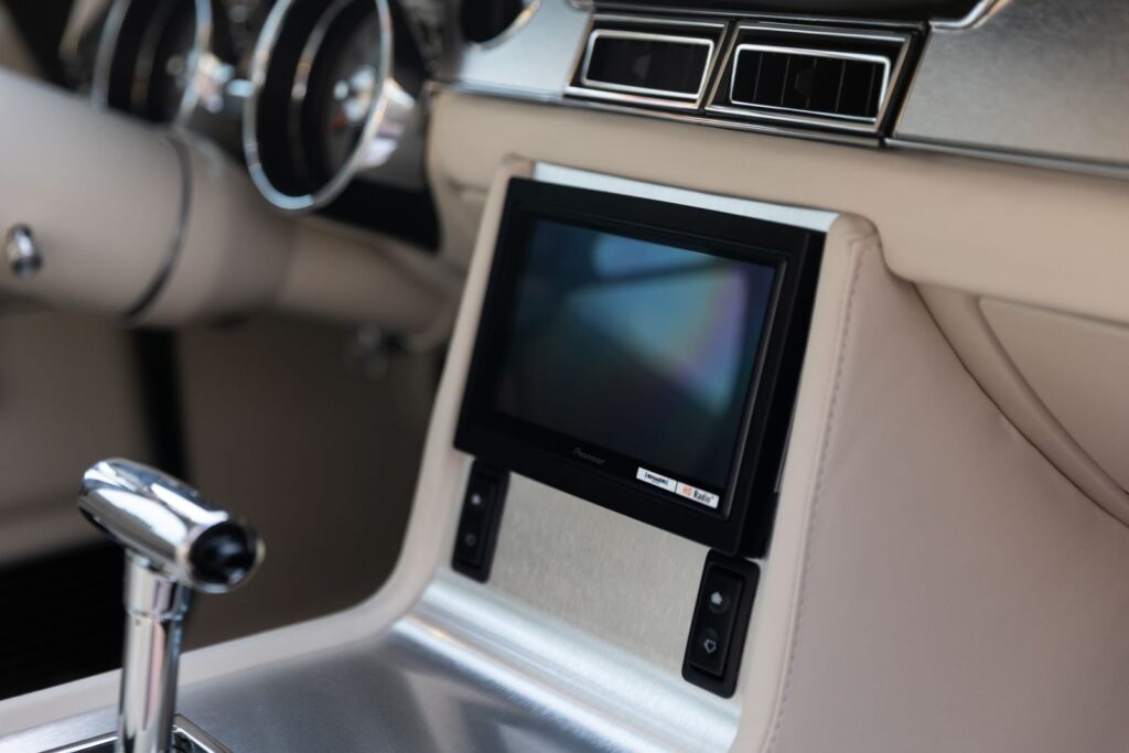 Close-up of a flush-mounted touchscreen infotainment system on a custom off-white leather center stack in a 1967 Revology Shelby GT350.