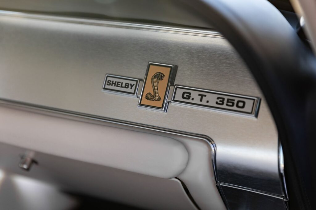 Extreme close-up of the "Shelby G.T. 350" dash emblem and Cobra snake logo mounted on brushed aluminum trim in a Revology 1967 Shelby.