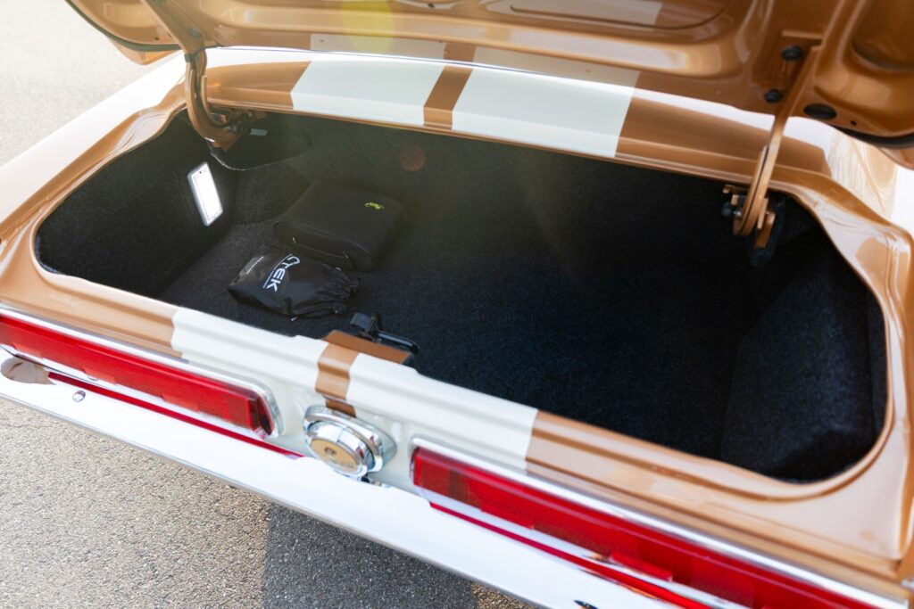 Open trunk of a Copper metallic 1967 Revology Shelby GT350 featuring premium black carpeting, integrated LED lighting, and white Le Mans racing stripes continuing onto the jamb.