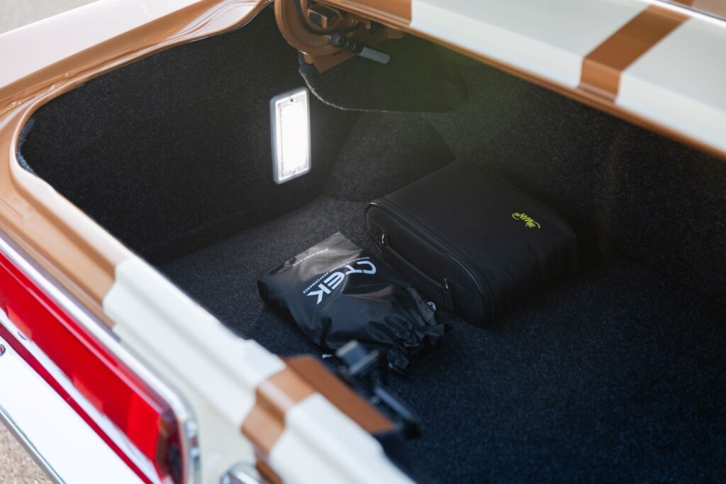 Close-up of the carpeted trunk area in a Copper metallic 1967 Revology Shelby GT350, featuring a bright LED cargo light and a CTEK battery maintainer kit.