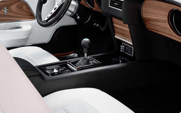 Close-up of the hand-wrapped leather center console in a Revology 1969 Mustang Boss 429, featuring a manual shifter, integrated modern power window switches, and parchment white leather bucket seats.