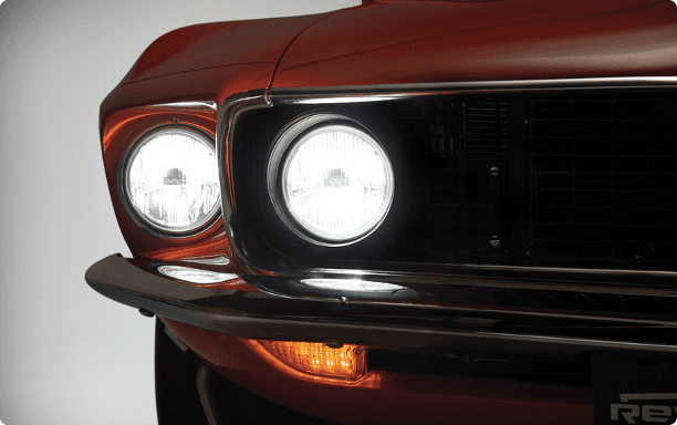 Close-up of the front grill and LED headlights of a 1969 Revology Mustang Boss 302 restomod, showing high-intensity illumination and premium chrome trim.