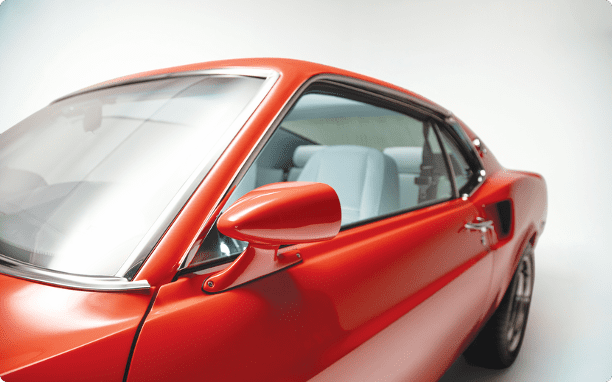 Exterior close-up of a Revology 1969 Mustang fastback in orange, featuring modern aerodynamic side mirrors and seamless power window glass integration.