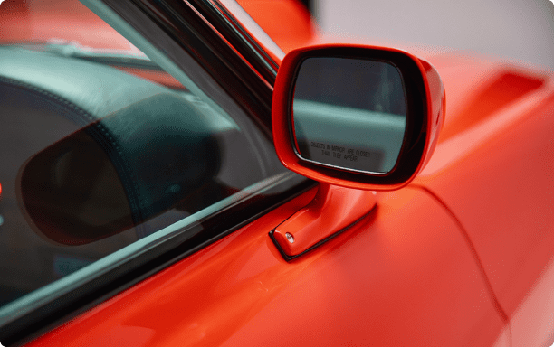 Close-up of a body-colored power side mirror on a 1969 Revology Mustang Boss 302, featuring an aerodynamic design and "objects in mirror are closer than they appear" safety glass.