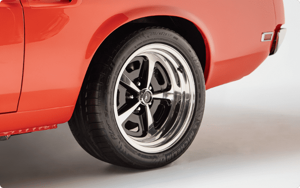Close-up of a 17-inch Magnum 500 wheel with a black and chrome finish, mounted with a Michelin Pilot Sport 4S tire (size 275/40 ZR 17) on a classic orange Ford Mustang.