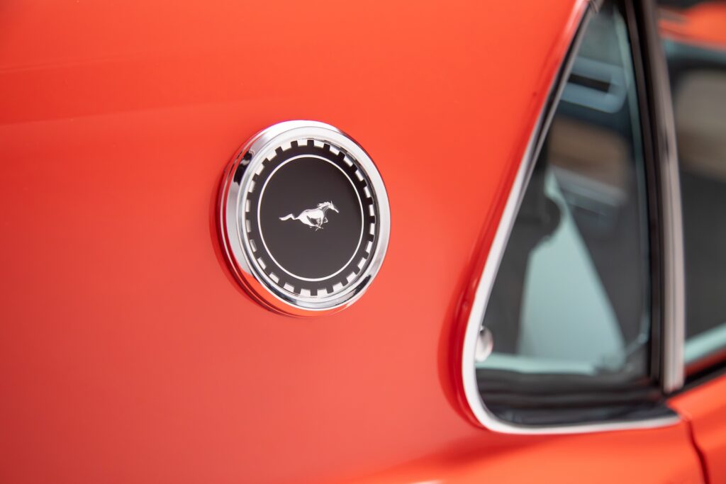 Close-up of the chrome Mustang "Running Horse" C-pillar emblem on a Revology 1969 Boss 429 restomod, featuring vibrant orange paint and polished quarter window trim.