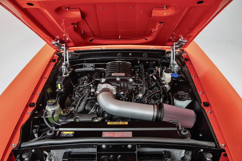 High-angle view of the engine bay in a Revology 1969 Ford Mustang Boss 429 restomod, showcasing a supercharged 5.0L Coyote V8 engine with a Roush supercharger, silver high-flow intake, and modern aluminum cooling system.