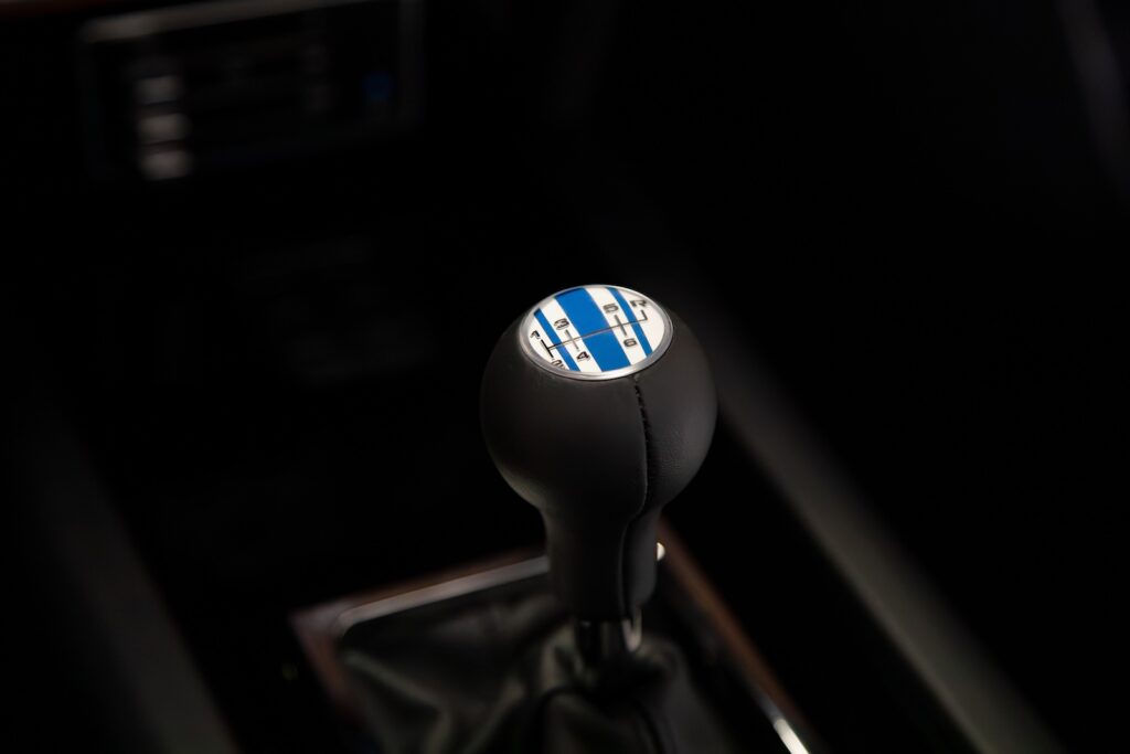 Close-up of the 6-speed manual gear shifter in a Revology 1969 Boss 429 Mustang restomod, featuring a black leather knob with a custom blue and white racing stripe gear pattern emblem.