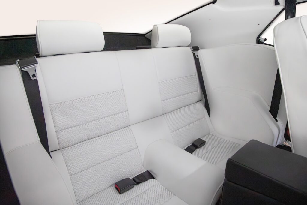 High-angle view of the rear bench seats in a Revology 1969 Ford Mustang Boss 429, featuring parchment white leather upholstery, adjustable headrests, and modern three-point retractable seatbelts.