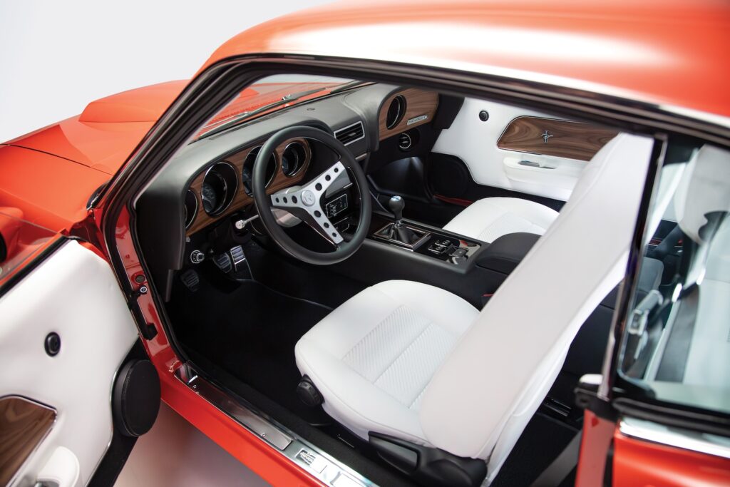 High-angle wide view of the custom interior in a Revology 1969 Ford Mustang Boss 429, featuring parchment white leather seats, a black leather-wrapped dashboard with walnut wood grain, and a bespoke center console.