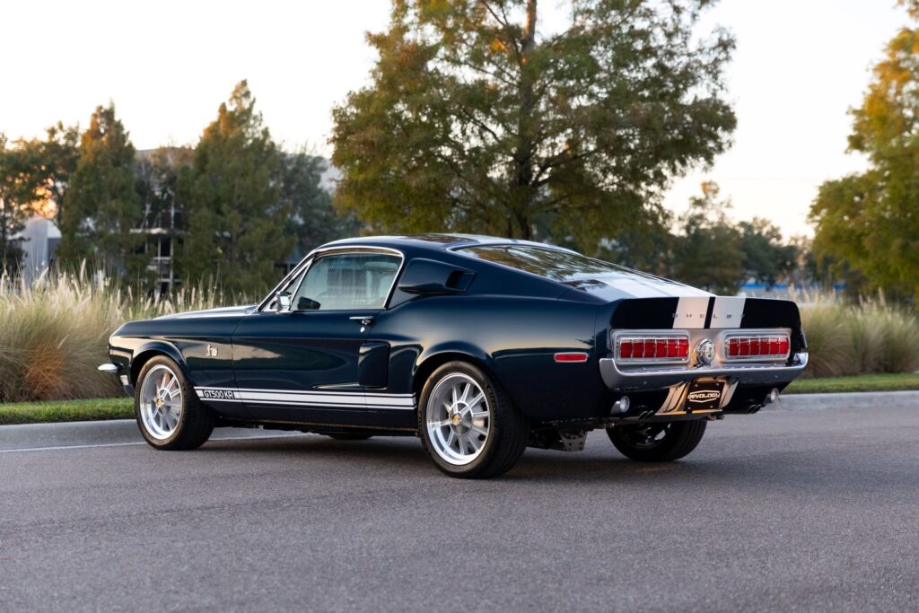 Rear three-quarter view of a dark green 1968 Revology Shelby GT500KR Fastback, highlighting the sequential horizontal taillights and integrated rear spoiler.