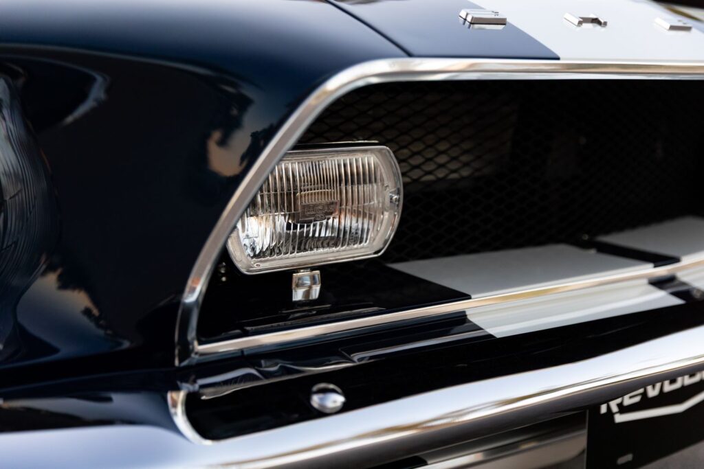 Close-up of the rectangular outboard fog light and black mesh grille on a 1968 Revology Shelby GT500KR with dark green metallic paint and chrome trim.