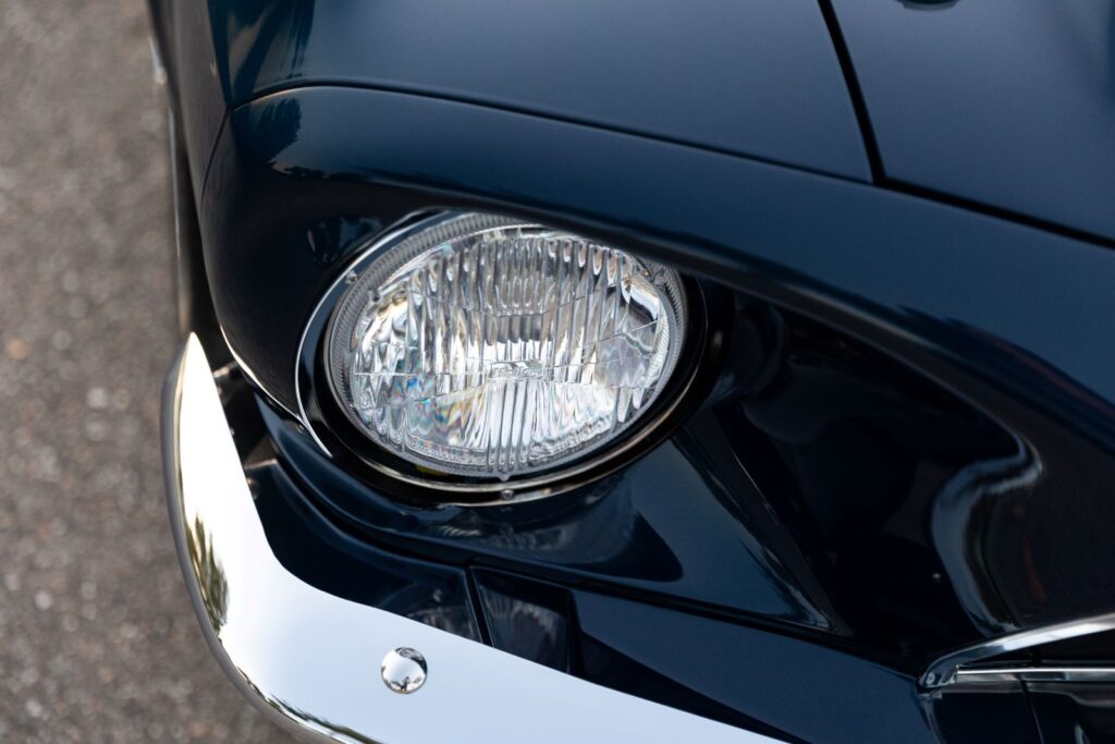 Close-up of the round headlight and chrome trim ring on a dark green 1968 Revology Shelby GT500KR, showing the smooth paint finish on the fender extension.