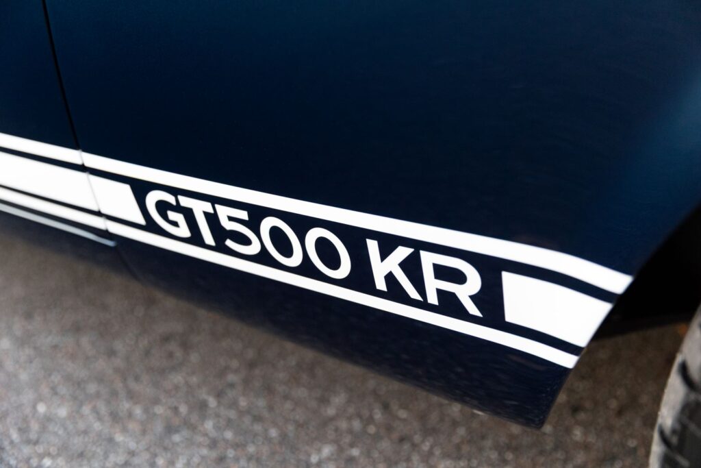 Close-up of the white "GT500 KR" rocker panel stripes on a dark green 1968 Revology Shelby Mustang.