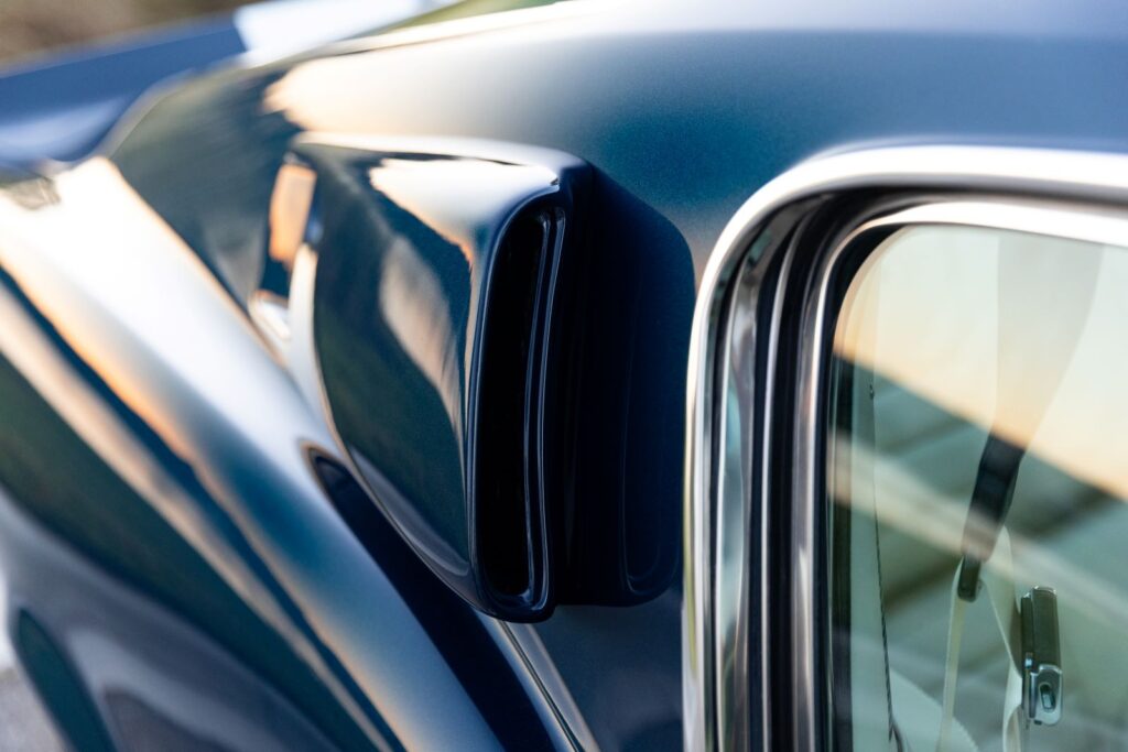 Macro view of the integrated C-pillar side air scoop on a dark green 1968 Revology Shelby GT500KR Fastback, showing the chrome window trim and metallic paint.