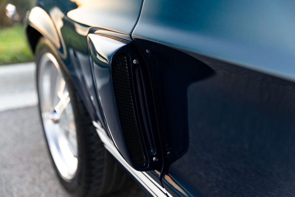 Close-up profile of the lower rear side scoop on a dark green 1968 Revology Shelby GT500KR, featuring a black mesh screen and integrated body lines.