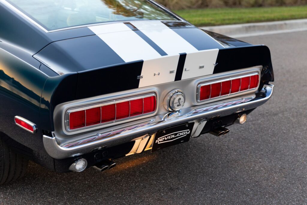 Rear-view close-up of a 1968 Revology Shelby GT500KR Fastback, showing the horizontal sequential taillights, white Le Mans stripes, and chrome Cobra gas cap.