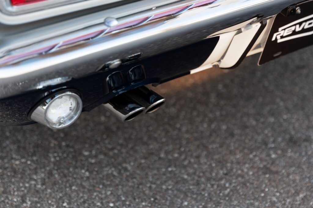 Close-up of the polished dual exhaust tips and round reverse light on the rear valance of a dark green 1968 Revology Shelby GT500KR.