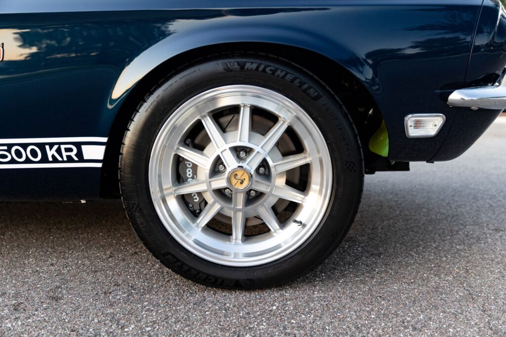 Side view of a 10-spoke polished alloy wheel on a 1968 Revology Shelby GT500KR, featuring a large Wilwood brake caliper and Michelin tires.