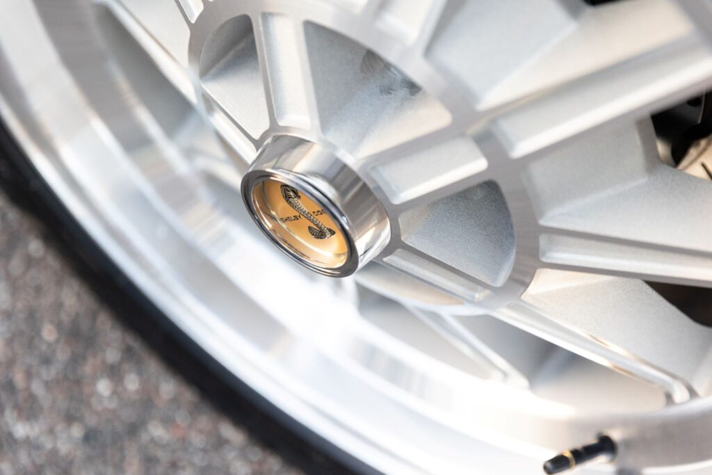 Extreme close-up of a gold Shelby Cobra snake emblem on the center cap of a polished 10-spoke alloy wheel for a 1968 Revology GT500KR.