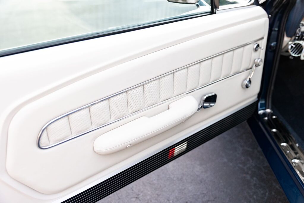 Interior view of a custom white leather door panel in a 1968 Revology Shelby GT500KR, featuring chrome trim accents and a black lower carpeted section.