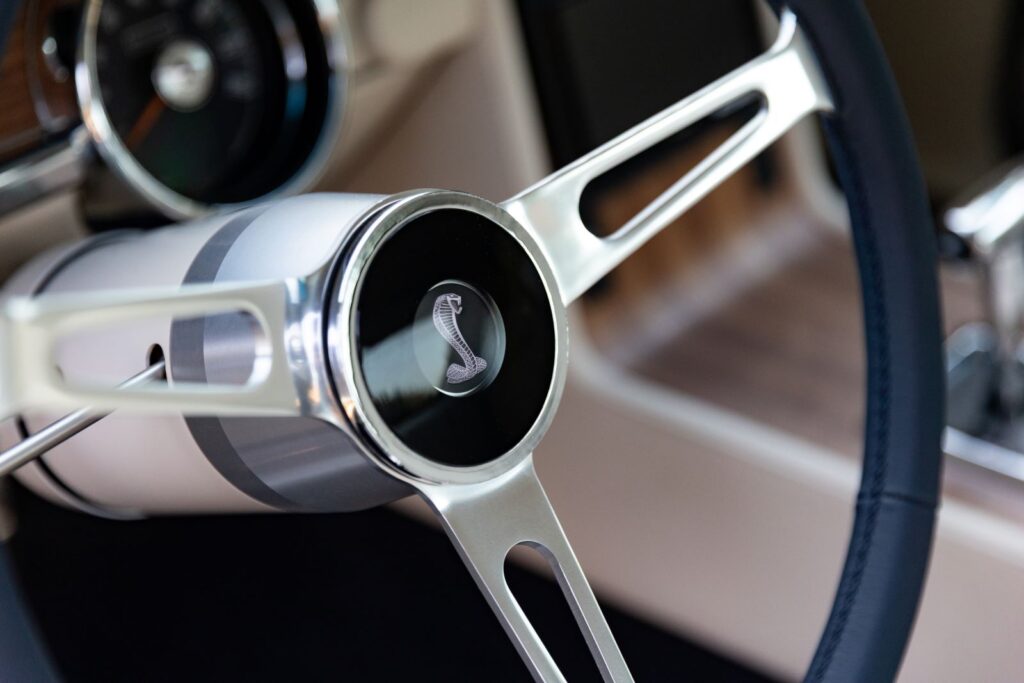 Extreme close-up of the polished aluminum three-spoke steering wheel hub with a black Shelby Cobra snake horn button in a 1968 Revology GT500KR.