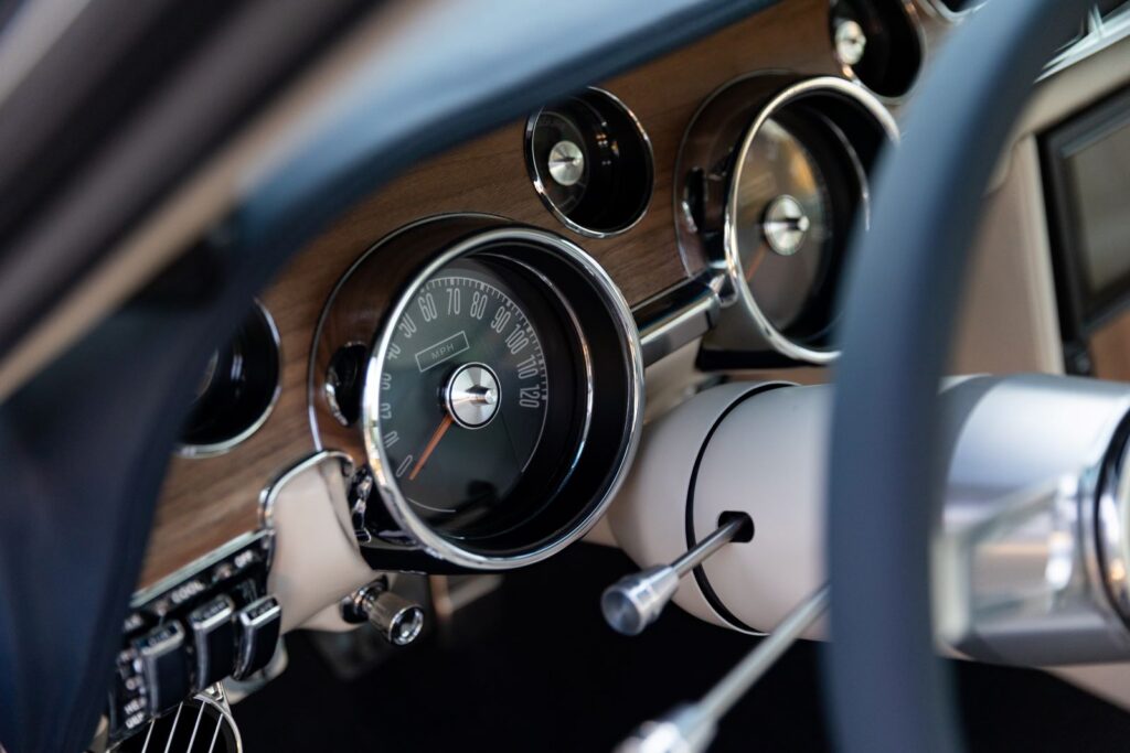 Close-up of the analog speedometer and wood grain instrument cluster in a 1968 Revology Shelby GT500KR, featuring chrome-rimmed gauges.